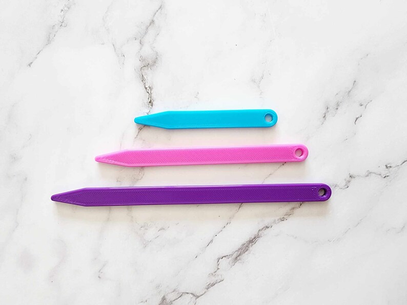 May include: Three plastic knitting needles in different sizes. The needles are purple, pink, and blue.