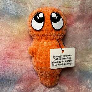 May include: Orange crocheted worry worm plush toy with big black eyes and a white tag that reads "I'm a snuggly worry worm. Cuddle me close and tight. Tell me all your worries and fears. I'll keep you safe day and night."