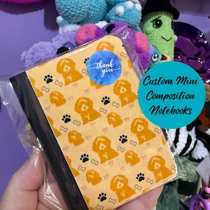 May include: A mini composition notebook with a yellow cover featuring a repeating pattern of orange dog illustrations, black paw prints, and white bones. A blue sticker with the words "thank you" is on the cover. The text "Custom Mini Composition Notebooks" is also visible.