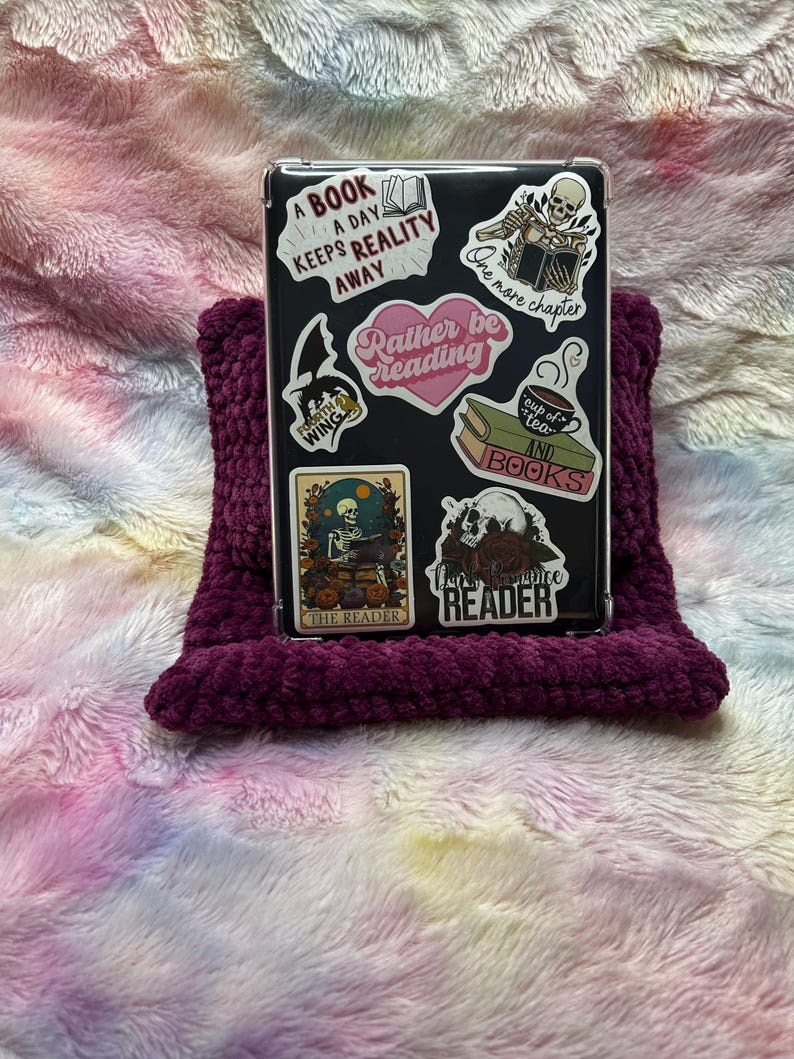 Op de afbeelding: Een transparante telefoonhoes met verschillende kleurrijke stickers met citaten over lezen. De stickers bevatten "Een boek per dag houdt de realiteit weg", "Liever lezen", "Nog een hoofdstuk", "Kop thee en boeken", "De lezer" en "De vraatzuchtige lezer".