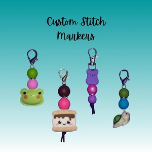 May include: Four colourful stitch markers with different charms. The charms include a frog, a s'more, a bear, and a turtle. The markers are attached to silver clips and have colourful beads.