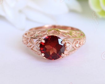 May include: A rose gold ring with a red gemstone and small clear gemstones set in a delicate filigree design.