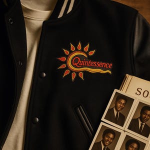 Op de afbeelding: Zwarte varsityjas met een "Quintessence" patch in rood en geel. De jas heeft zwarte leren mouwen en een wit en zwart gestreepte kraag. Een stapel vintage foto's is zichtbaar.