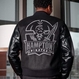May include: Black varsity jacket with a gray leather sleeve and a gray embroidered logo on the back that says "Hampton Pirates".
