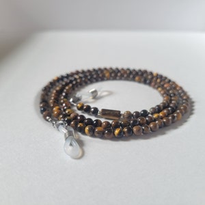May include: A beaded eyeglass chain made of small, round, tiger's eye stones. The chain has silver-colored metal loops to attach to glasses and a small rectangular tiger's eye bead. The chain is brown and gold.