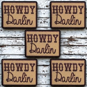 May include: Five rectangular embroidered patches with a tan background and a dark brown border. Each patch features the text "HOWDY" in a bold, blocky font above the word "Darlin" written in a cursive script, both in dark brown thread.