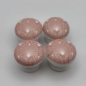 May include: Four decorative cabinet knobs. Each knob has a round, pink and white patterned top with a white base. The pattern is a stylized, symmetrical design. These knobs are suitable for adding a decorative touch to furniture.