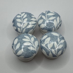 May include: Four ceramic cabinet knobs. Each knob is round with a white leaf pattern over a blue background. These knobs are likely for furniture or decorative use.