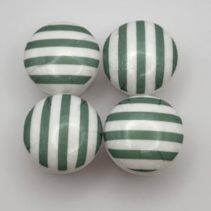 May include: Four round cabinet knobs with a white base and green horizontal stripes. The knobs are evenly spaced against a white background. The knobs are likely made of ceramic or a similar material.