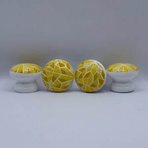 Peut inclure: Quatre boutons de meuble d&eacute;coratifs. Chaque bouton a une base blanche et un motif de mosa&iuml;que jaune sur le dessus. Le motif de mosa&iuml;que utilise diff&eacute;rentes nuances de jaune. Les boutons sont dispos&eacute;s en rang&eacute;e sur un fond blanc.