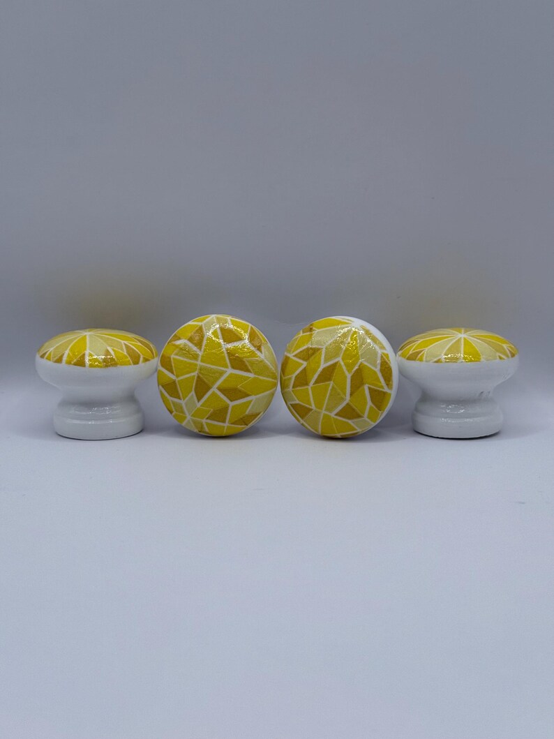 Peut inclure: Quatre boutons de meuble d&eacute;coratifs. Chaque bouton a une base blanche et un motif de mosa&iuml;que jaune sur le dessus. Le motif de mosa&iuml;que utilise diff&eacute;rentes nuances de jaune. Les boutons sont dispos&eacute;s en rang&eacute;e sur un fond blanc.