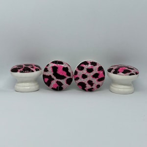 May include: Four white ceramic cabinet knobs with a pink and black leopard print design.