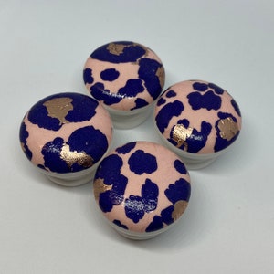 May include: Four round pink and blue decorative knobs with a gold metallic pattern. The knobs have a white base.