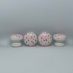 May include: Four pink wooden drawer knobs with a colourful raindrop pattern.