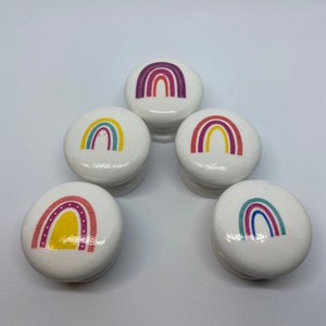 May include: Five white round wooden knobs with rainbow designs. Each knob features a different rainbow design with various colours, including yellow, red, blue, green, and purple.