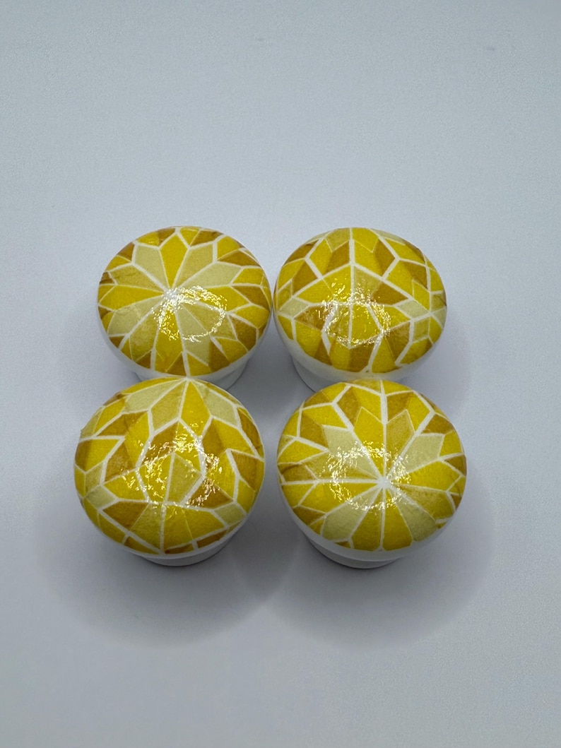 Peut inclure: Quatre boutons de meuble ronds avec un motif de mosa&iuml;que dans les tons de jaune et de blanc. Les boutons ont un motif g&eacute;om&eacute;trique et sont pos&eacute;s sur un fond blanc. Ces boutons d&eacute;coratifs peuvent &ecirc;tre utilis&eacute;s pour les meubles ou d'autres projets de d&eacute;coration int&eacute;rieure.