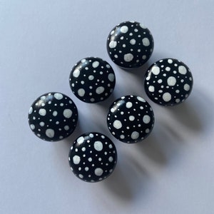 May include: Six black round knobs with white polka dots. The knobs are painted with a white polka dot pattern on a black background.