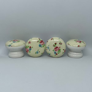 May include: Four white ceramic knobs with a floral pattern in shades of pink, blue, and green. The knobs have a rounded top and a short, cylindrical base.
