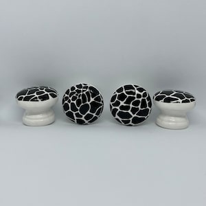 May include: Four white ceramic cabinet knobs with a black and white animal print design.