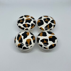 May include: Four round, white ceramic knobs with a brown and black leopard print design.