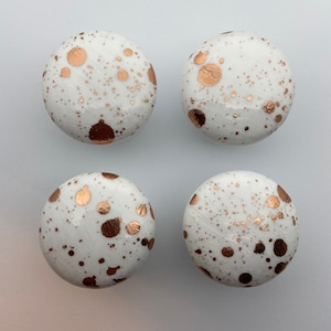 May include: Four white round knobs with a speckled gold paint design.