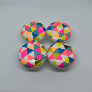 May include: Set of four colourful wooden knobs with a geometric pattern of pink, blue, green, and yellow triangles.