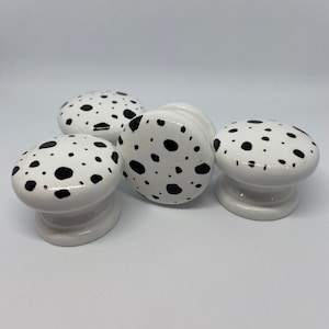 May include: Four white ceramic cabinet knobs with black polka dot patterns.