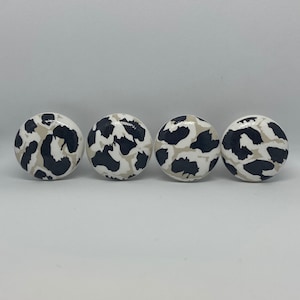 May include: Four round, white ceramic knobs with a black and beige leopard print design.