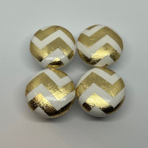 May include: Four round wooden knobs with a white background and gold chevron pattern.