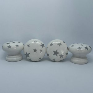 May include: Four white ceramic cabinet knobs with a silver star pattern.
