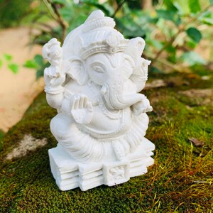 May include: White Ganesha statue with a detailed design, sitting on a base with multiple layers. The statue is made of a smooth, white material and has a serene expression.