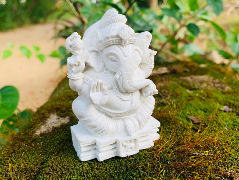 May include: White Ganesha statue with a detailed design, sitting on a base with multiple layers. The statue is made of a smooth, white material and has a serene expression.