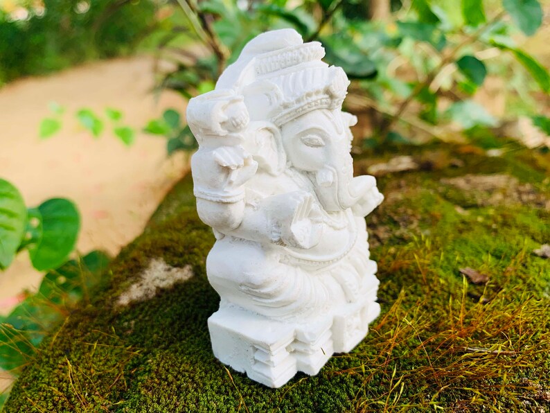 May include: White Ganesha statue with intricate details, sitting on a bed of moss. The statue is made of a smooth, white material and has a traditional design.