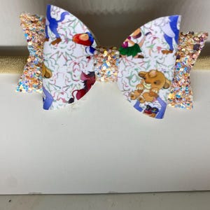 May include: A white and blue patterned bow featuring cartoon characters. The bow has glittery gold accents and is attached to a gold headband. The bow showcases characters from a well-known animated film.