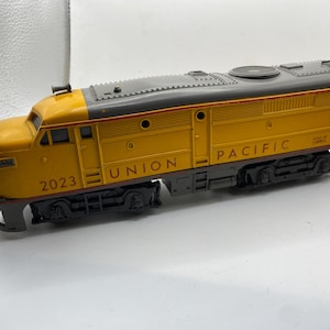 May include: A yellow and grey Union Pacific model train with the number 2023 on the front. The train has black wheels and the words "UNION PACIFIC" are printed on the side. The model train is a collectible item.