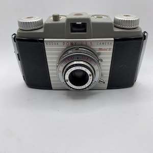Puede incluir: Una cámara vintage Kodak Pony 135 Modelo B. La cámara tiene una parte superior gris y una parte frontal plateada con laterales negros. La lente es de 51 mm f/4.5. El texto "Kodak Pony 135 Camera" está impreso en la parte delantera.