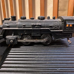Può includere: Una locomotiva a vapore giocattolo nera con caldaia dettagliata, ruote con bielle metalliche e il numero 400 stampato sul lato della cabina. Il modello include un camino, cupole sulla parte superiore e una piccola finestra laterale.