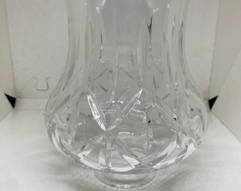 May include: A clear, cut-glass vase with a flared top and a rounded base. The vase features a diamond-cut pattern around the base and a vertical cut design on the upper portion. The vase sits on a small, circular foot.