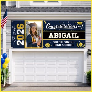 May include: A navy blue graduation banner with the text "Class of 2026" and "Congratulations!" features a photo of a graduate. The banner also includes the graduate's name, "ABIGAIL", and "SOUTH SHORE HIGH SCHOOL". An American flag and balloons are also visible.