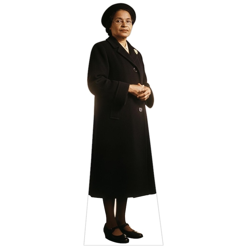 May include: A life-size cardboard cutout of Rosa Parks standing and facing forward. She is wearing a long black coat, a matching black hat, and dark-rimmed glasses. Her hands are clasped in front of her, and she wears black shoes on her feet.