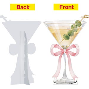 May include: A double-sided cardboard cutout featuring a martini glass illustration. The front displays a yellow cocktail with four green olives on a pick and a pink ribbon tied around the stem. The back is plain white with a fold-out support stand.