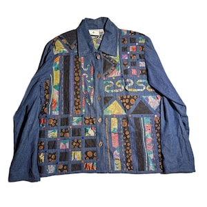 May include: A long-sleeved denim jacket featuring a patchwork front panel with a mix of blue denim, black fabric with brown circles, and multi-colored floral patterns. The jacket has a collared neckline, a button-down front, and long sleeves.