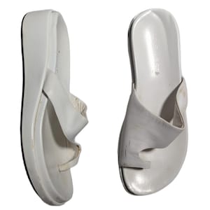 May include: A pair of white Nine West platform sandals featuring a thong-style toe post design. The sandals have a thick wedge sole and a wide strap across the top of the foot. The brand name Nine West is printed on the heel of the footbed.