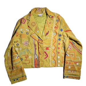 May include: Olive green blazer with colorful embroidered details. The jacket features a notched collar, three buttons, and intricate patterns in red, blue, orange, and white. The embroidery includes geometric shapes and floral motifs.