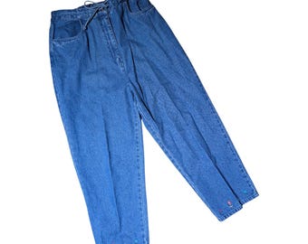 May include: High-waisted blue denim jeans featuring a drawstring waist closure, two front pockets, and small, colourful embroidered flower motifs along the bottom hems of the pant legs. The denim has a medium blue wash with a relaxed fit silhouette.