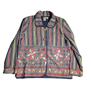 May include: A long-sleeved jacket featuring a dark blue base with vertical stripes in shades of green, pink, and white. The lower section displays a geometric star pattern in pink, white, and black, finished with three round wooden buttons.
