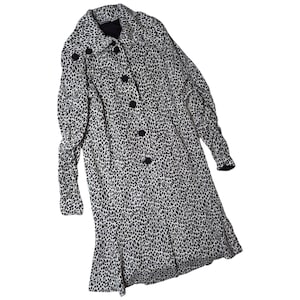 May include: A long-sleeved coat featuring a black and white leopard print pattern. The coat has a wide collar, a front button closure with five black circular buttons, and a slightly flared hemline. The fabric displays a consistent animal print.