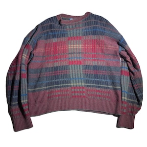 May include: A maroon, blue, and gray plaid sweater. The sweater has a ribbed hem and cuffs, and a crew neck. The plaid pattern is made up of vertical and horizontal stripes in varying widths. The sleeves are long and the sweater appears to be made of a soft knit material.