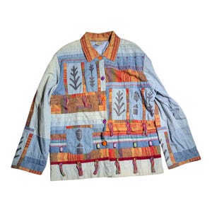 Puede incluir: Chaqueta vaquera azul claro con diseño patchwork. La chaqueta presenta varios patrones geométricos y abstractos en tonos naranja, rojo y gris. Tiene cuello, cierre de botones y borlas decorativas.