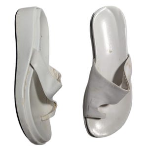 Puede incluir: Par de sandalias de plataforma Nine West de cuero blanco. Las sandalias tienen una correa para el dedo del pie tipo tanga y una suela gruesa ligeramente curvada. Las sandalias están diseñadas para uso casual y tienen una estética minimalista.